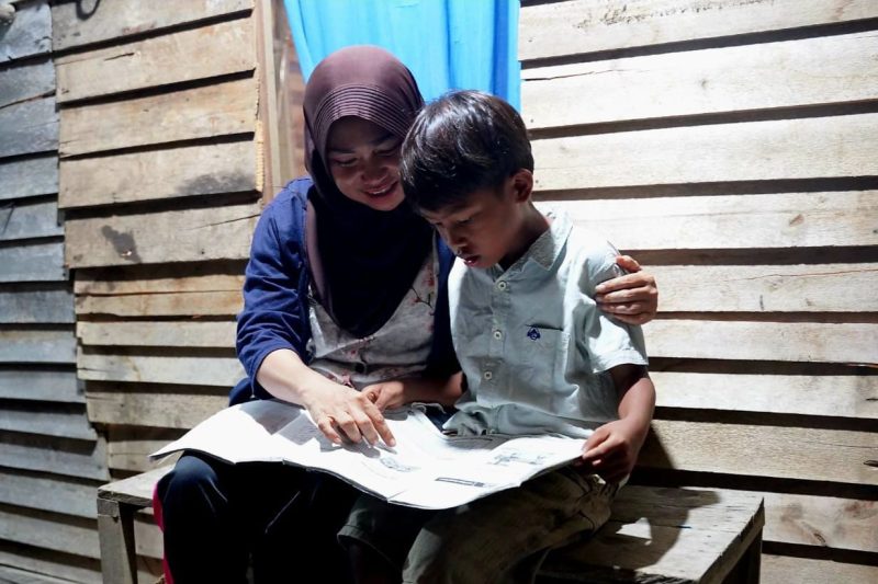 Wiwik Handayani (kiri), warga Sungai Kunyit, Mempawah, Kalimantan Barat sedang menemani anaknya belajar di rumahnya pada malam hari pascadirinya menerima bantuan penyambungan listrik gratis melalui program Light Up The Dream PLN.